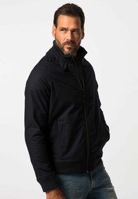 Marinblå bomberjacka med hög krage, dragkedja och ribbade muddars. Har två framfickor med subtila texturerade paneler.