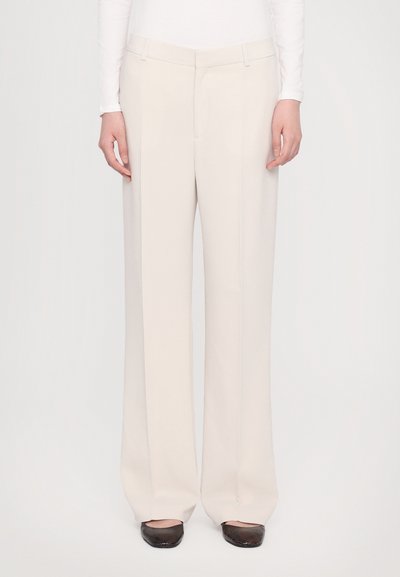 Pantalons larges en tissu beige léger, avec une taille plate, des poches latérales et une coupe ajustée. Texture lisse et lignes épurées.