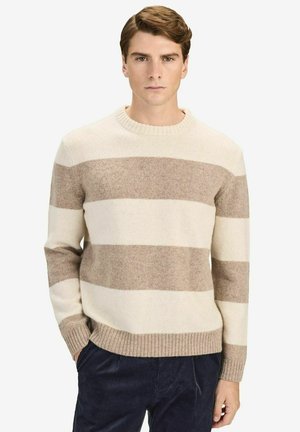 Beige och gräddfärgad randig tröja i mjuk stickad kvalitet, med rund hals och ribbade manschetter och fåll, bärs över mörka kordbyxor.