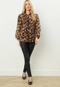 Blusa marrone e nera a motivo, con bottoni frontali, pieghe e maniche a palloncino, abbinata a leggings neri lucidi e tacchi a punta.