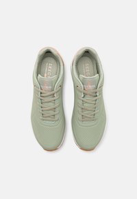 Green athletic shoes with a textured upper, featuring perforations, textured laces, and a light-colored sole. Brand logo on tongue.