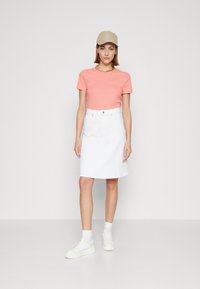 Lys rosa ribbet kortermet topp kombinert med et hvitt denimskjørt og hvite sneakers. En beigefarget caps gir et tilbehør som detalj.
