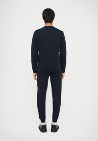 Felpa blu navy e pantaloni coordinati realizzati in tessuto morbido. La felpa ha un collo rotondo e polsini a coste; i pantaloni presentano caviglie elastiche.