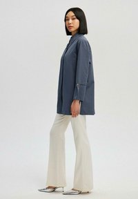 Blue long-sleeve shirt, buttoned, relaxed fit, paired with cream flared pants and silver pointed-toe heels. Smooth fabric, minimal design.