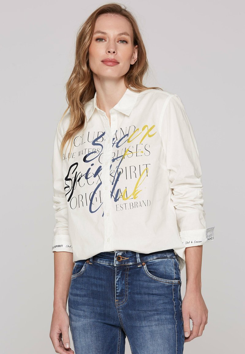 Witte blouse met een kleurrijk tekstontwerp in marineblauw, geel en zwart. Lange mouwen, casual pasvorm, met merkgebonden manchetdetails.
