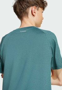 Tyrkysové športové tričko s textúrovanou látkou, krátkymi rukávmi a okrúhlym výstrihom. Na zadnej strane sa nachádza diskrétne logo CLIMACOOL.