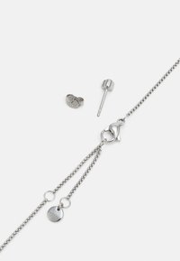 Silver smyckeset som inkluderar ett kedjehalsband med en kräfta lås, en cylindrisk studörel och en texturerad ring med en logotyp.