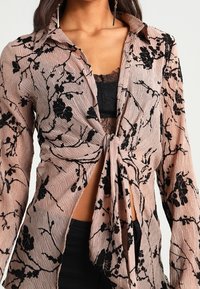 Blusa rosa leggera con motivo floreale, dotata di un design con fiocco davanti e maniche lunghe, caratterizzata da un tessuto testurizzato e una sottoveste in pizzo.