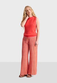 Röd ärmlös stickad topp kombinerad med vida randiga byxor i röd och vitt. Slät textur med en avslappnad passform och bekväma sandaler.