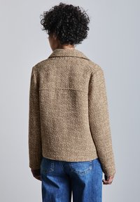 Hnědá strukturovaná bunda s límcem, dlouhými rukávy a rovný střih. V kombinaci s modrými džínami. Jednoduchý design bez ozdob.