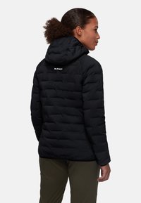 Giacca nera isolata con cappuccio, caratterizzata da un design trapuntato e un logo bianco sul retro. Il materiale appare liscio e opaco.
