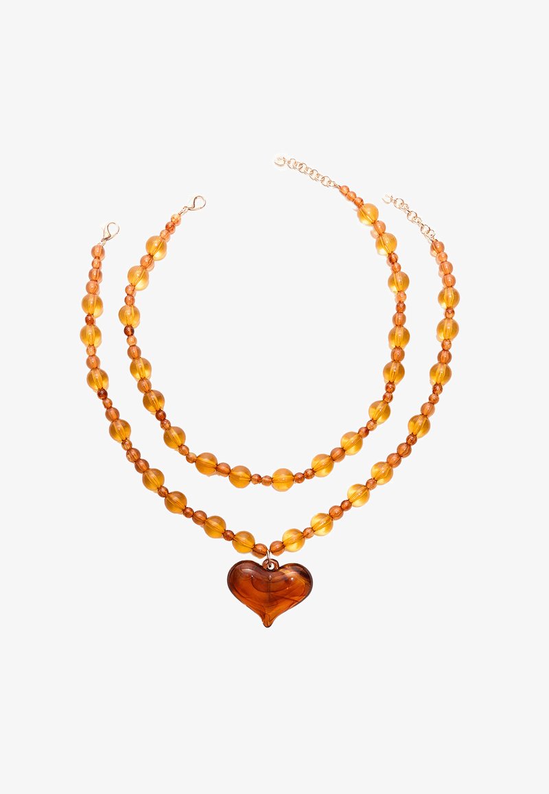 Collana a due strati con perle di colore ambra di varie dimensioni, con un grande pendente a forma di cuore al centro. Chiusura e dettagli in tonalità oro.