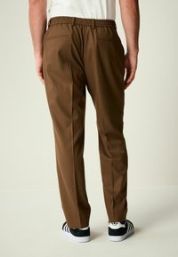 Pantaloni marroni con vita elastica, due tasche posteriori, design a gamba dritta e scarpe da ginnastica bianche e nere. Tessuto dalla texture liscia.