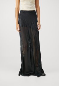 Jupe maxi noire avec un design en couches comprenant des panneaux transparents et texturés, ornée d'une ceinture à perles et d'un élégant tombé.