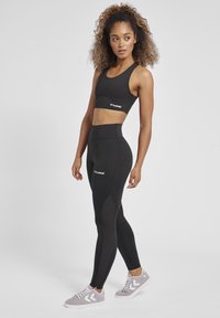 Svart sport-bh och högmidjade leggings med mesh-detaljer, tillverkade av stretchigt tyg. Grå träningsskor med vit logotypdetalj.