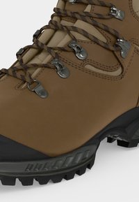 Καφέ πεζοπορικό μποτάκι με επενδυμένη γλώσσα, μεταλλικά ανοίγματα για κορδόνια, σχεδιασμένα κορδόνια, ενισχυμένη μύτη και στιβαρή μαύρη λαστιχένια σόλα.