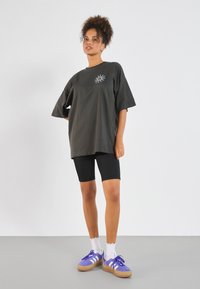 Dark gray oversized t-shirt with short sleeves and sun graphic, paired with black bicycle shorts, white socks, and purple sneakers.
