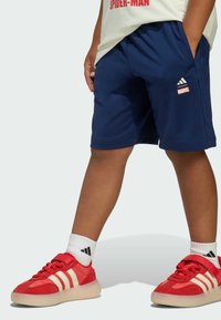 Námornícke šortky adidas s elastickým pásom, bočnými vreckami a malým červeným logom "MARVEL". Skombinované s červenými teniskami s bielymi pruhmi.