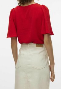 Rød tekstureret kortærmet top parret med en højtlivet hvid denimnederdel med en slids bagpå og to påsyede lommer. Logoetiket på taljebåndet.