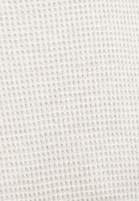 Tecido texturizado em forma de waffle em cinza claro, com um padrão de grelha. O material parece macio e respirável, adequado para vestuário casual ou uso doméstico.