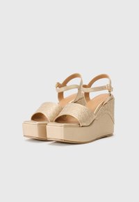 Sandales à talons compensés dorées avec un dessus texturé et à motifs, une conception à bout ouvert et une sangle de cheville réglable. Semelle plateforme avec un léger éclat.