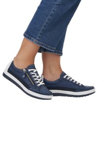 Baskets bleues avec diverses textures, dotées d'une fermeture éclair sur le côté, de lacets blancs et d'une semelle blanche. Conçues avec une esthétique sportive et décontractée.
