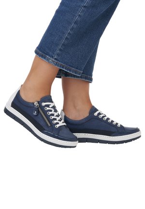 Baskets bleues avec diverses textures, dotées d'une fermeture éclair sur le côté, de lacets blancs et d'une semelle blanche. Conçues avec une esthétique sportive et décontractée.
