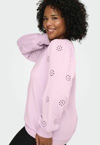 Svetlo vijoličasta jopa z nabranimi rokavi in vzorci izrezanih cvetov. Mehka tkanina z rebrastimi manšetami in robom, oblikovana za udobje.