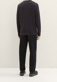 Maglione a maglia testurizzata blu navy con collo a giro, abbinato a pantaloni neri e stivaletti neri alla caviglia. Focus sui dettagli dei polsini e dell'orlo a coste.