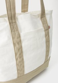 Lerret toteveske med beige stropper og bunn. Har en frontlomme og forsterkede, sydd håndtak. Fargekombinasjon: hvit og beige.