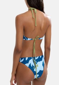 Dwuczęściowy bikini w niebieskim kolorze z białym wzorem kwiatowym; halterka z wiązaniami w kolorze zielonym; dolna część typu low-rise z minimalnym pokryciem i bocznymi wiązaniami.