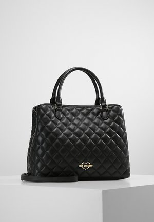 Black quilted leather handbag with double handles, gold "Love Moschino" logo, and detachable shoulder strap on white pedestal.