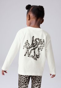 Camisa de manga larga color crema con un diseño gráfico de estampado de leopardo negro en la espalda. Combinada con pantalones a juego con patrón de leopardo.