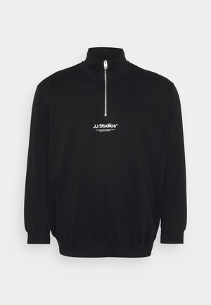 Sudadera negra de cuello alto, con media cremallera y puños acanalados. Presenta un pequeño logo blanco en el pecho. Textura suave.