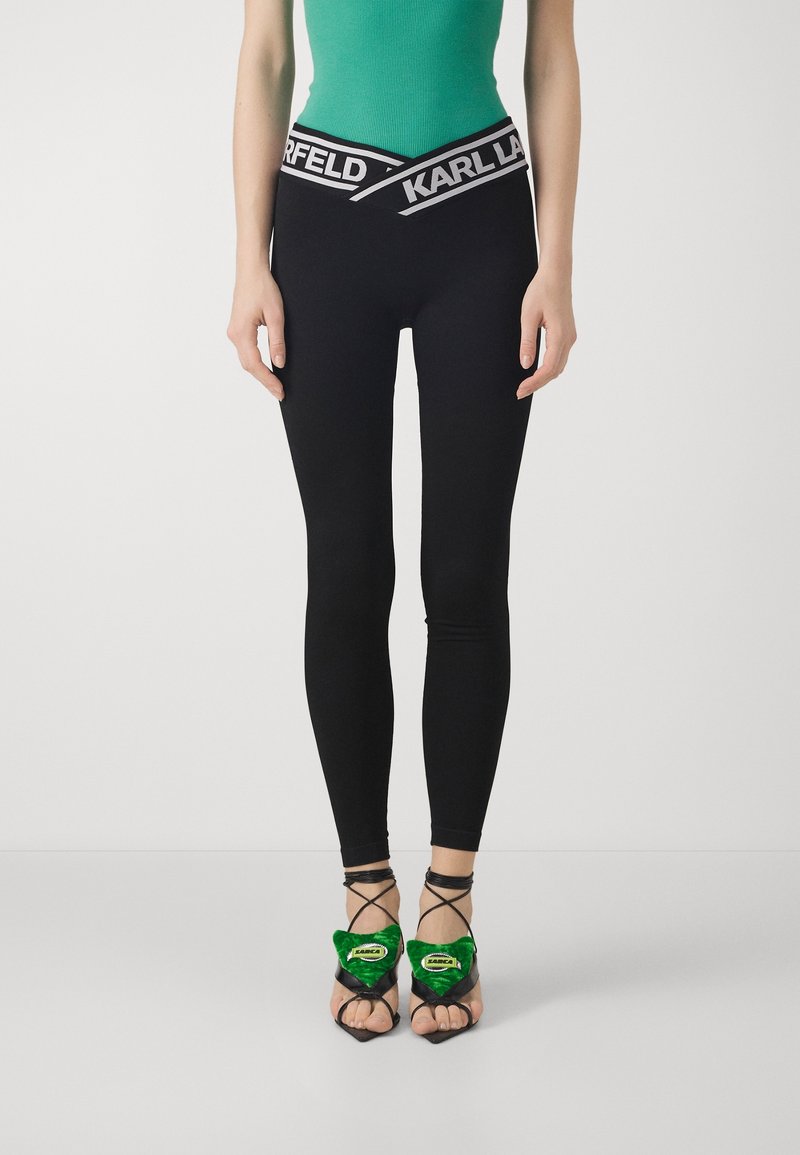Zwarte leggings met een brede tailleband met daarop "KARL LAGERFELD" in het wit. Gecombineerd met zwarte sandalen met groene fluwelen accenten en enkelbandjes.