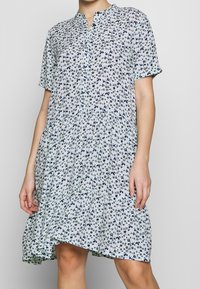 Hellblaues Hemdblusenkleid mit kurzen Ärmeln, versehen mit einem Navy-Blumenmuster. Ausgestellt geschnitten, aus leichtem Stoff gefertigt.