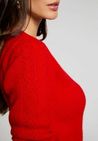 Maglione rosso lavorato a maglia con un design testurizzato e dettagli decorativi sulle maniche, realizzato in un materiale morbido e leggero.