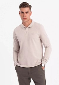 Polo shirt a maniche lunghe color beige chiaro con tessuto testurizzato, logo discreto sul petto e design del colletto classico.