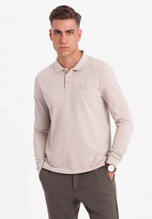Polo shirt a maniche lunghe color beige chiaro con tessuto testurizzato, logo discreto sul petto e design del colletto classico.