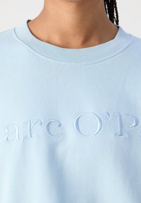 Light blue sweatshirt featuring a ribbed neckline and embroidered text "Marc O'Polo" on the front, made from soft cotton material.