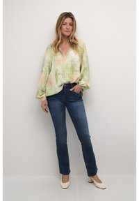 Zelená a broskvová abstraktně vzorovaná blůza s výstřihem do V, dlouhými rukávy a gumičkovými manžetami, spárovaná s tmavomodrými slim-fit džínami a béžovými podpatky.