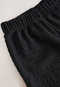 Pantalon en tissu noir texturé avec taille élastique présenté sur une surface plane et claire.