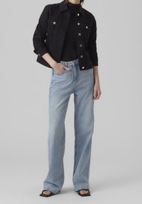 Black denim jacket with silver buttons, paired with light blue wide-leg jeans. Black fitted top underneath and black heeled sandals.