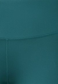 Tissu côtelé bleu sarcelle avec une taille haute, doté de coutures plates et d'une texture lisse. Aucun logo ou motif visible.