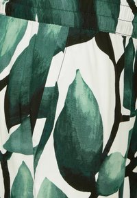 Zelená a bílá tkanina s velkými vzory listů. Hladká textura, elastický pas a skládané detaily.