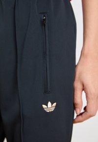 Námornícky športové nohavice majú zipsovú kapsu a logo adidas v ružovom zlate. Sú vyrobené z hladkého, ľahkého materiálu.