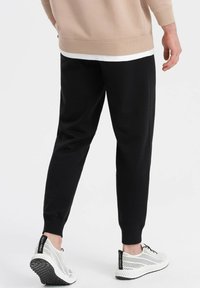 Schwarze tapered Jogginghosen mit gerippter Textur und elastischen Bündchen, kombiniert mit weißen perforierten Sneakers mit schwarzen Akzenten.