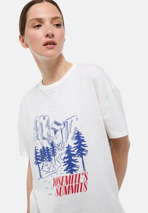 T-shirt en coton blanc avec un motif bleu de Yosemite comprenant des arbres et des montagnes, agrémenté d'un texte rouge indiquant "LES SOMMETS DE YOSEMITE."