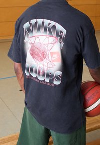 Czarny t-shirt z krótkim rękawem z grafiką obręczy koszykarskiej oraz napisem "NIKE HOOPS SUMMER LEAGUE" w niebieskich i różowych literach.