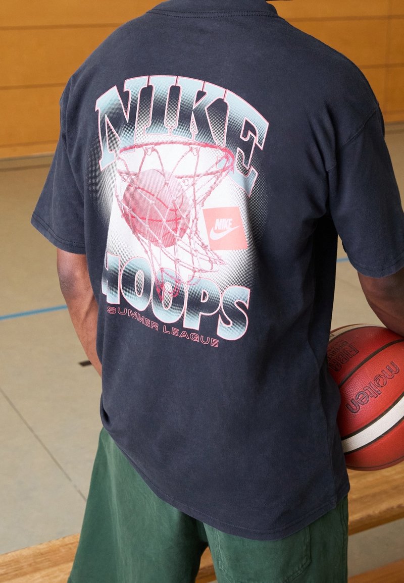 Czarny t-shirt z krótkim rękawem z grafiką obręczy koszykarskiej oraz napisem "NIKE HOOPS SUMMER LEAGUE" w niebieskich i różowych literach.